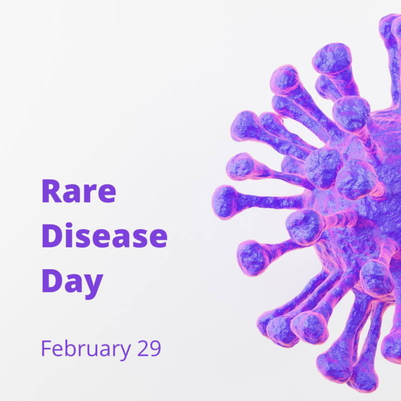 The illustration features a detailed, purple depiction of a virus or bacteria cell against a light background. The cell has various protrusions extending from its center. To the left of the cell, bold purple text reads “Rare Disease Day.” Below, in smaller font but still bold and purple, the date “February 28” is indicated. The overall design aims to raise awareness about rare diseases and their impact.