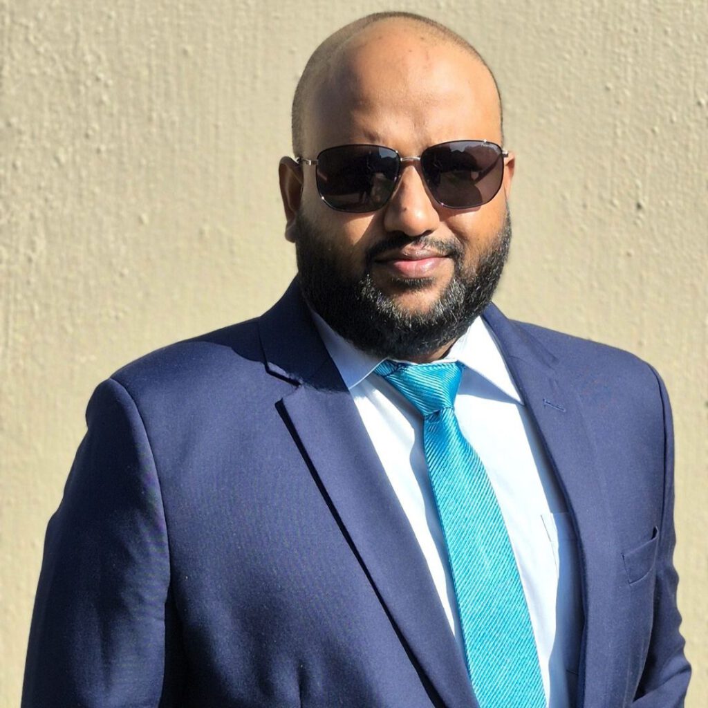 Manny pictured wearing a dark blue suit and a light blue tie