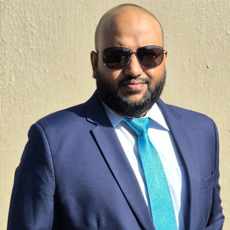 Manny pictured wearing a dark blue suit and a light blue tie