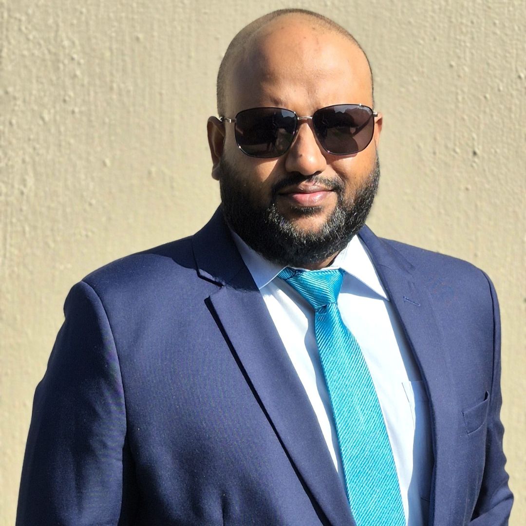 Manny pictured wearing a dark blue suit and a light blue tie