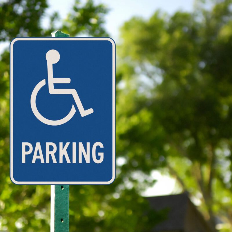 Disability parking sign with a white wheelchair symbol and the word "PARKING" in bold, all on a blue rectangular background with a white border.