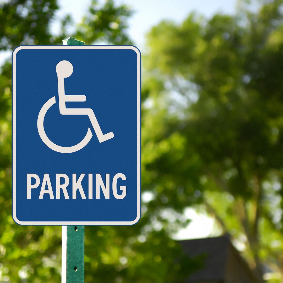 Disability parking sign with a white wheelchair symbol and the word "PARKING" in bold, all on a blue rectangular background with a white border.