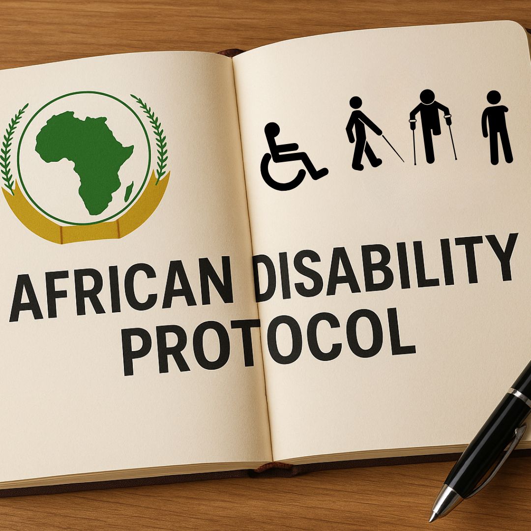 An open notebook on a wooden surface displays the title "African Disability Protocol" in bold black letters. On the left page is a green silhouette of the African continent encircled by a golden emblem with laurel leaves, and on the right is a black disability icons. A black pen lies beside the notebook