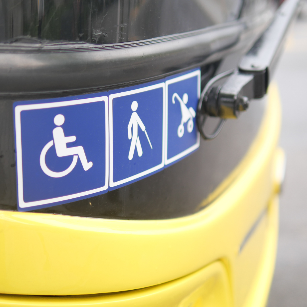 Close-up of three blue accessibility signs on a yellow public transport vehicle: a wheelchair symbol, a person with a cane symbol, and a stroller symbol