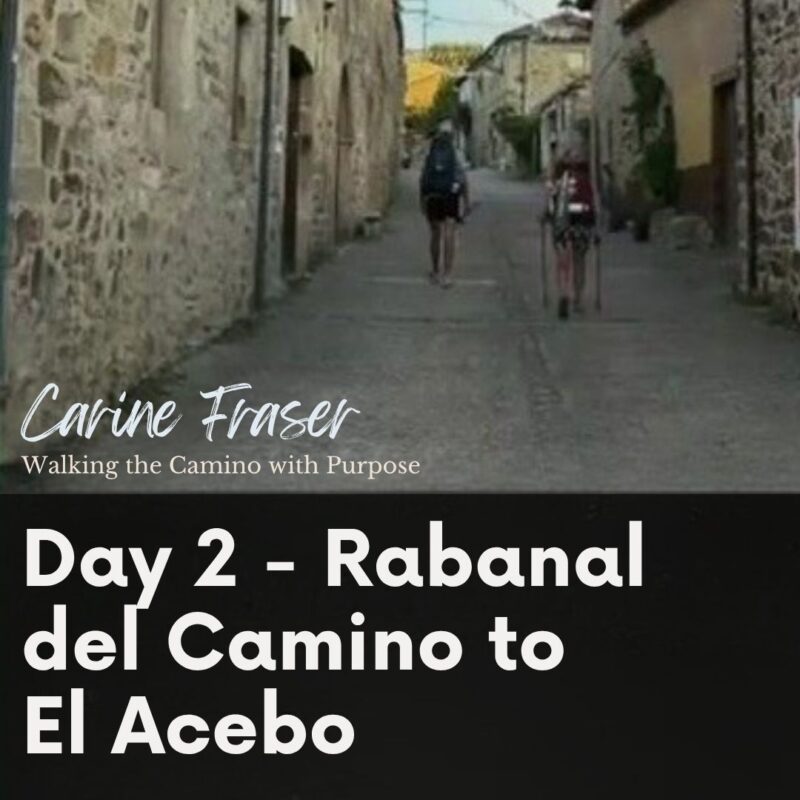 Two pilgrims with backpacks walking away from the camera along a narrow stone-paved street in El Acebo, flanked by traditional stone buildings. Text overlay reads "Carine Fraser – Walking the Camino with Purpose" and "Day 2 – Rabanal del Camino to El Acebo."