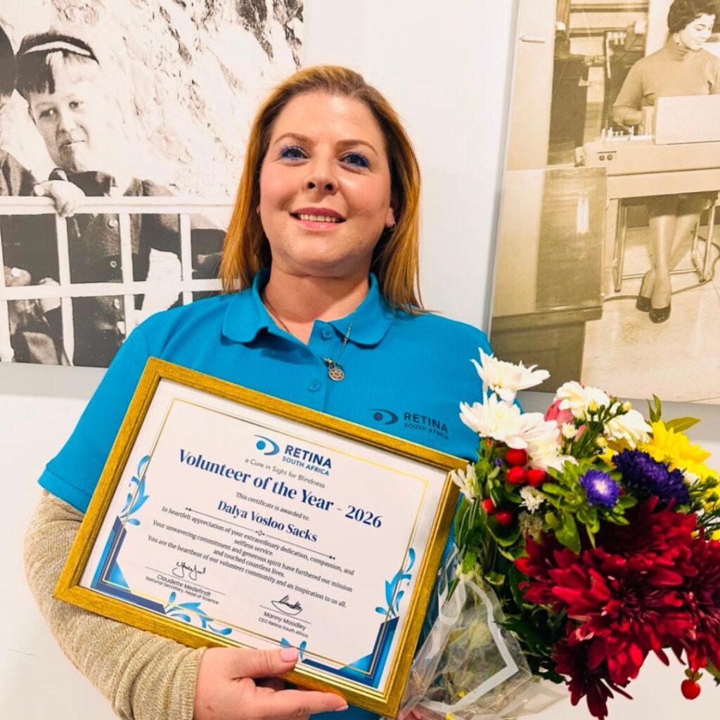 Dalya Vosloo-Sacks smiling and holding her framed Retina South Africa Volunteer of the Year 2026 certificate and a bouquet of flowers, standing in the Retina South Africa office